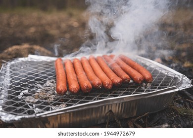 Grilling sausages on disposable instant grill. Grilling pickniking in nature surrouned by forest trees and pines
