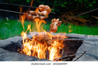 Grilling sausages over a campfire. Grilling food over flames of bonfire on wooden branch - stick spears in nature at night. Scouts way of preparing food. Campfire in the garden. - Powered by Shutterstock