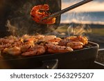 Grilling shrimp outdoors at sunset by the seaside with smoke rising into the air