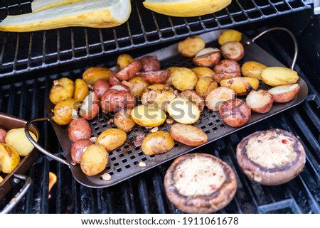 Grilling small potatoes with slices of garlic on an outdoor gas grill.