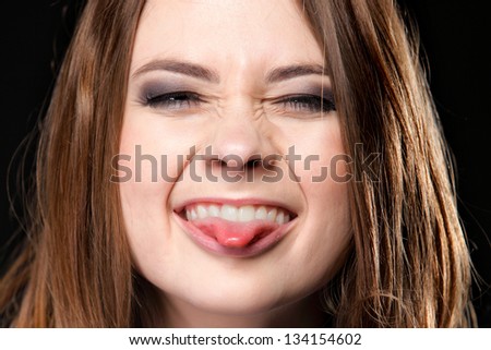 Grimacing young woman making silly face sticking out her tongue on black background