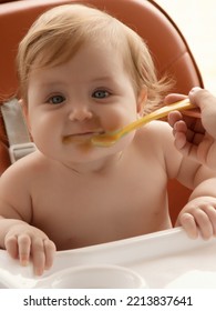 Grimy Child Eats With Hands Sitting On Table At Home. Little Smiling Girl Sits In Baby-chair And Have A Breakfast. Baby With Big Eyes And Red Curly Hair Eats At A Table. Summer Vacation Concept