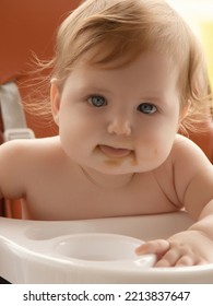 Grimy Child Eats With Hands Sitting On Table At Home. Little Smiling Girl Sits In Baby-chair And Have A Breakfast. Baby With Big Eyes And Red Curly Hair Eats At A Table. Summer Vacation Concept