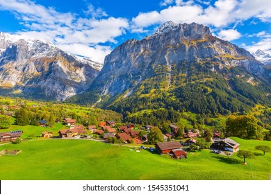 Grindelwald, Switzerland aerial village view and autumn Swiss Alps mountains panorama landscape, wooden chalets on green fields and high peaks in background, Bernese Oberland, Europe