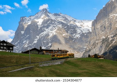 In Grindelwald, the train gently winds through alpine chalets, beneath the towering snow-capped peaks, carrying travelers into the heart of a breathtaking landscape. Switzerland 🇨🇭 - Powered by Shutterstock