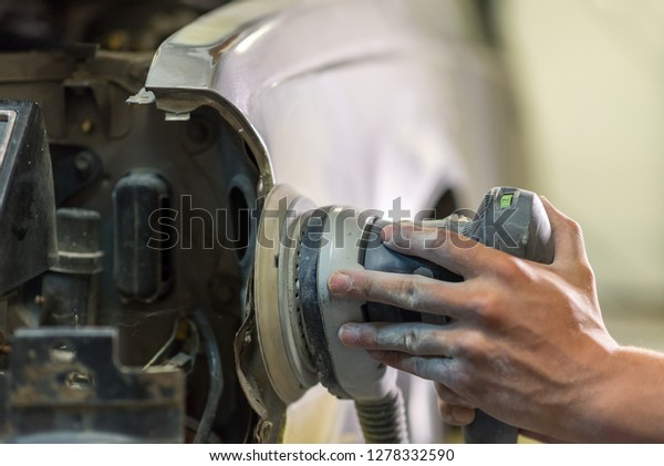 Grinder in the hands of a man who sharpen a car\
varnish in the car\
shop.