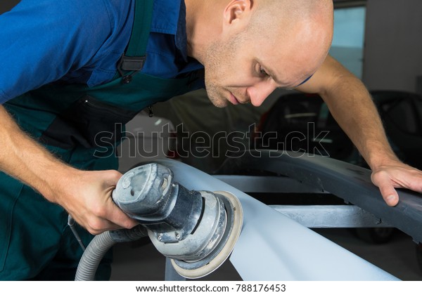 Grinder in the hands of a man who sharpen a car\
varnish in the car\
shop.