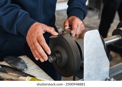 grinder sharpens the knife by holding it in hands on the abrasive rotating wheel of the sharpening machine in workshop - Powered by Shutterstock