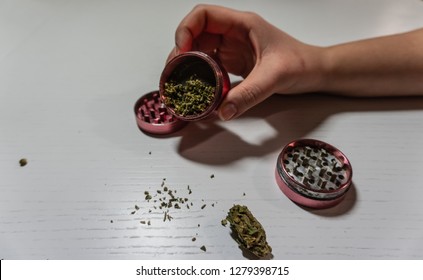 Grinder in woman hand. Medical marijuana buds in crasher. Cannabin on white table (background)