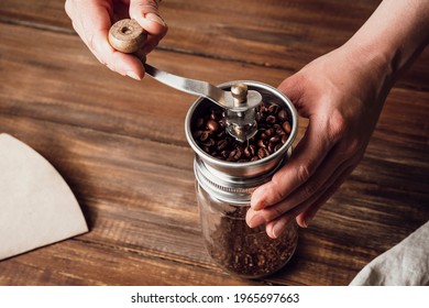 Grinding coffee beans in a manual coffee grinder on a wooden table - Powered by Shutterstock