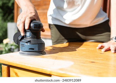 Grinding with an electric wood grinder, restoration of solid wood furniture. Woodwork. Close up of sanding a wood with orbital sander at workshop - Powered by Shutterstock