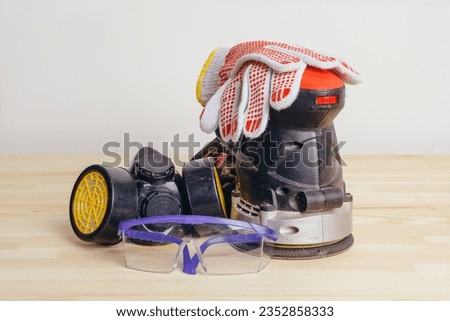 Grinding machine, gloves, goggles and a protective mask on a wooden table against a white wall.
