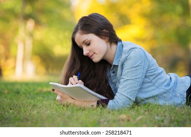 Grinning young woman writing on notebook outdoors