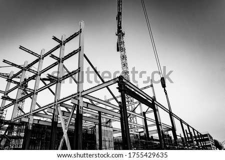 Gritty construction image of steel framing and construction crane on building site in monochrome.