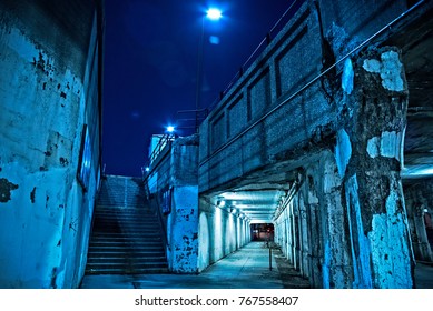 Gritty Dark Chicago City Street Under Industrial Bridge Viaduct Tunnel With A Stairway To Metra Train Station At Night.