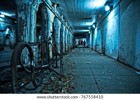 Gritty dark Chicago city street under industrial train bridge viaduct tunnel with bicycle and person at night.