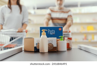 Groceries on the checkout counter conveyor belt and customers waiting in the background - Powered by Shutterstock