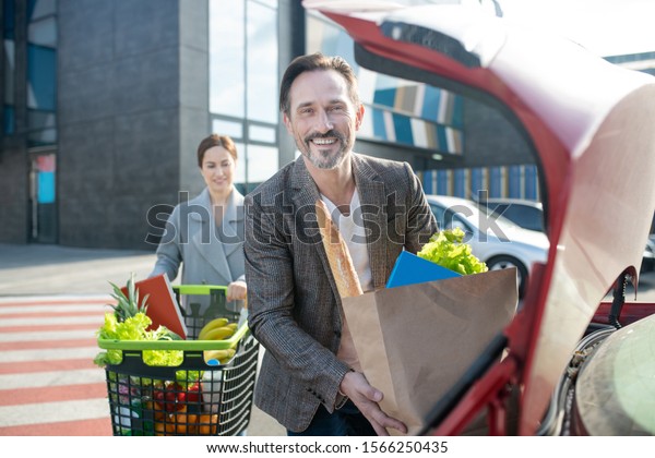 Groceries\
shopping together. Cheerful couple feeling happy after groceries\
shopping together while standing near\
car