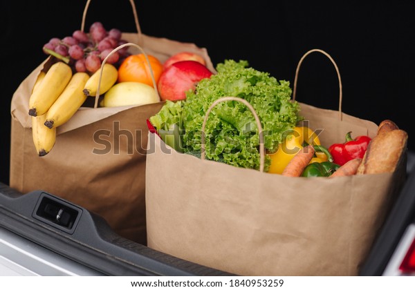 Groceries from a supermarket in a car trunk. Food\
delivery during quarantine. Cruft Paper eco bags for shopping.\
Fresh fruits and vegetables,\
vegan