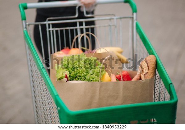 Groceries from a supermarket in a\
trolley outdoors. Food delivery during quarantine. Cruft Paper eco\
bags for shopping. Fresh fruits and vegetables,\
vegan