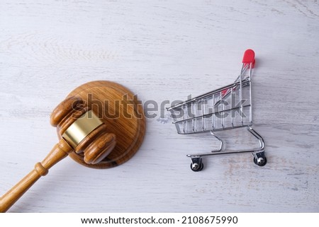 grocery cart and judge gavel on white brick wall background, consumer protection concept