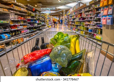 Grocery cart at a supermarket aisle filled up with food products seen from the customers point of view