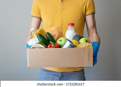 Grocery Donation. Concept Of Contact Less Delivery. Man In Gloves Holds Box Of Food. Donation Box With Food Supply, Canned Food, Cereals, Vegetables. Concept Of Food Delivery