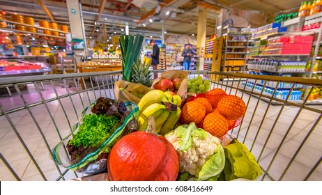 Grocery Shop Cart In Supermarket Filled Up With Fresh And Healthy Food Products As Seen From The Customers Point Of View With People Shopping In Background