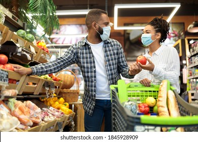 Grocery Shopping. African Family Couple In Masks Buying Vegetables Together Standing With Shop Cart In Supermarket Groceries Store Indoor. Buyers Choosing Healthy Food Concept