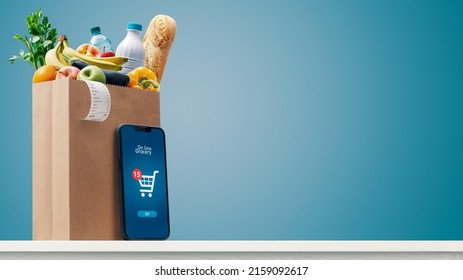 Grocery shopping app and grocery bag full of goods: online grocery shopping and home delivery concept, copy space - Shutterstock ID 2159092617