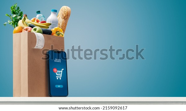 Grocery shopping\
app and grocery bag full of goods: online grocery shopping and home\
delivery concept, copy\
space