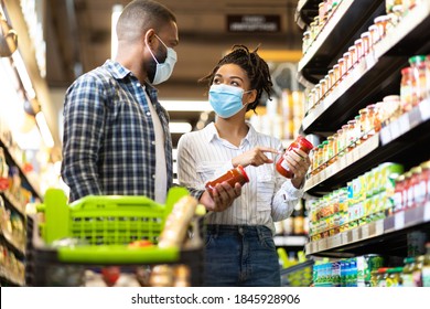 Grocery Shopping. Black Family Couple In Masks Buying Groceries In Supermarket Store Indoors. Buyers Standing With Shopping Cart In Aisles Choosing Food Products. Shop Safe During Covid-19 Pandemic