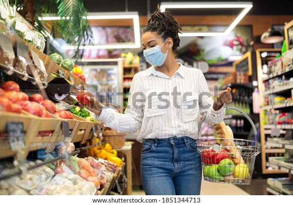 Grocery\
Shopping. Black Woman Choosing Fresh Vegetables In Supermarket,\
Walking With Basket Full Of Food Along Shelves In Store Aisle.\
Groceries Shop Sales And Discounts\
Concept