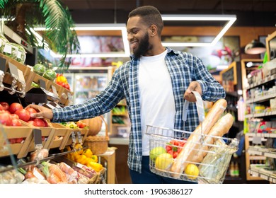 Grocery Shopping. Cheerful African American Guy In Supermarket Choosing Fresh Fruits And Vegetables, Carrying Basket Buying Natural Healthy Food In Modern Store. Selective Focus - Powered by Shutterstock