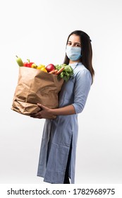 Grocery Shopping In Pandemic - Pretty Indian Young Woman Wearing Protective Mask While Holding Paper Bag With Vegetables And Fruits During Virus Epidemic