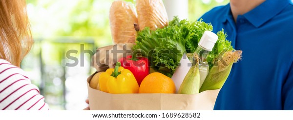 Grocery store delivery man\
in blue uniform delivering food to a woman customer at home, banner\
size