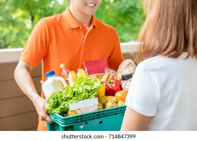 Grocery Store Delivery Man Wearing An Orange Polo-shirt Delivering Food To A Woman At Home