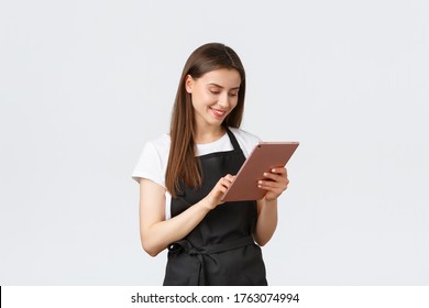 Grocery store employees, small business and coffee shops concept. Friendly cute female barista in black apron smiling at camera, using digital tablet to manage cafe orders - Powered by Shutterstock