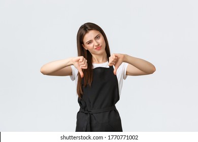 Grocery Store Employees, Small Business And Coffee Shops Concept. Skeptical And Disappointed Waitress In Black Apron Smirk Displeased And Showing Thumbs-down, White Background