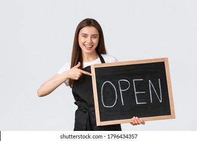 Grocery store employees, small business and coffee shops concept. Cheerful cute female barista in black apron pointing at open sign, inviting come enjoy drinks in cafe, standing white background - Powered by Shutterstock