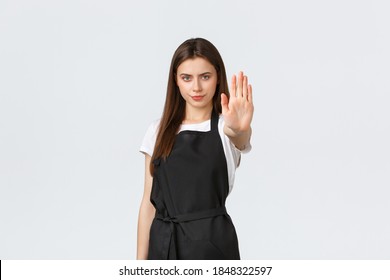 Grocery Store Employees, Small Business And Coffee Shops Concept. Serious Determined Female Barista Extend Hand To Say Stop, Restrict Or Prohibit Action, Standing In Black Apron