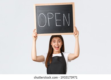 Grocery Store Employees, Small Business And Coffee Shops Concept. Cheerful Happy Barista In Black Apron Raise Open Sign, Inform Customers That Shop Or Cafe Working After Covid Pandemic