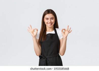 Grocery store employees, small business and coffee shops concept. Satisfied happy female barista in black apron showing okay sign and biting lip tempting. Pleased saleswoman recommend buy online