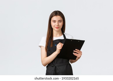 Grocery store employees, small business and coffee shops concept. Shop manager checking products in stock, writing down items on clipboard, wearing black apron uniform, white background - Powered by Shutterstock