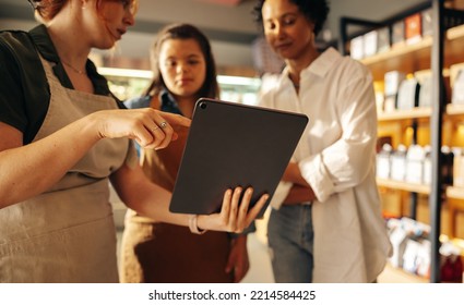 Grocery Store Manager Using A Digital Tablet While Having A Discussion With Her Employees In A Staff Meeting. Group Of Diverse Women Working Together In An All-female Small Business.