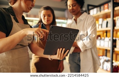 Grocery store manager using a digital tablet while having a discussion with her employees in a staff meeting. Group of diverse women working together in an all-female small business.