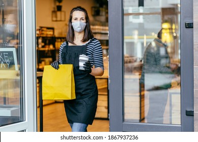 Grocery Store Owner Working Only With Take Away Orders During Coronavirus Outbreak. Young Woman Worker Wearing Face Protective Mask Giving Coffee To Customer. Healthcare And Food, Drinks Concept.