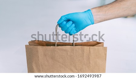 Grocery store shopping delivery man giving paper bag wearing blue glove as protection for COVID-19 Coronavirus precautions.