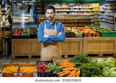 Grocery store worker in apron stands confidently with arms crossed. Surrounded by fresh produce like carrots and tomatoes in modern supermarket. Brightly lit store interior. - Powered by Shutterstock