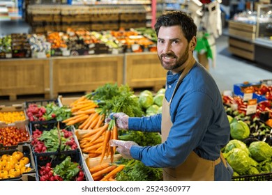 Grocery worker arranging fresh vegetables at supermarket, smiling while handling carrots. Surrounded by vibrant produce like tomatoes, radishes, and lettuce. Represents healthy eating - Powered by Shutterstock